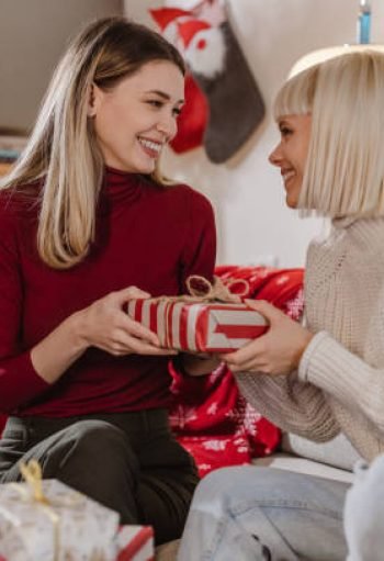 ift 2 Two young women are enjoying in living room during Christmas time, one of the is giving Christmas present to the other one